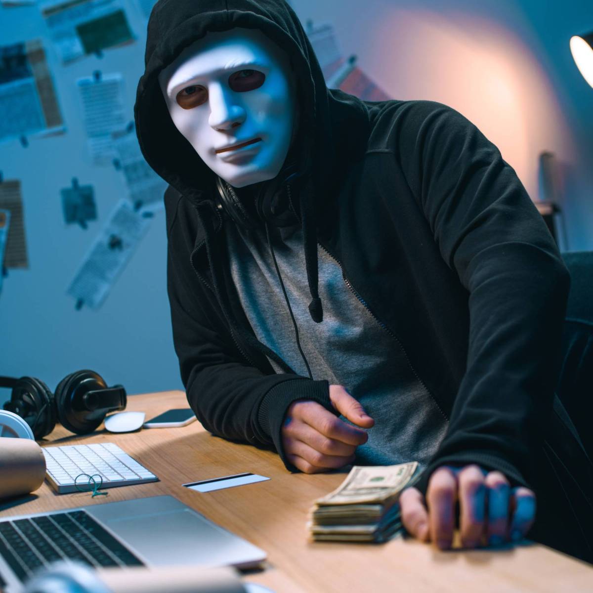 hacker in mask with stack of money on desk